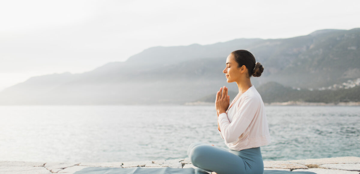 Young woman praying and meditating outdoors by seaside. Self care and mindfulness, menthal health. Awakening in morning